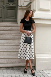 a lady in a black top and a white printed skirt